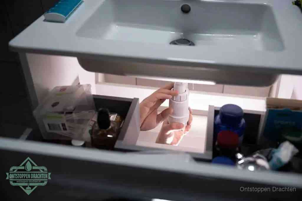 Een pompfles met zeep boven een wastafel, de heet water en afwasmiddel-methode om een vetprop in de afvoer los te maken in Drachten