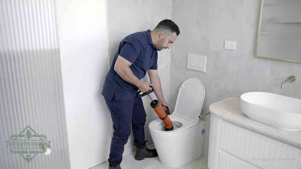 Een monteur buigt over een wandcloset en duwt met de hand een persluchtontstopper in de toiletpot om de verstopping handmatig los te maken in Drachten