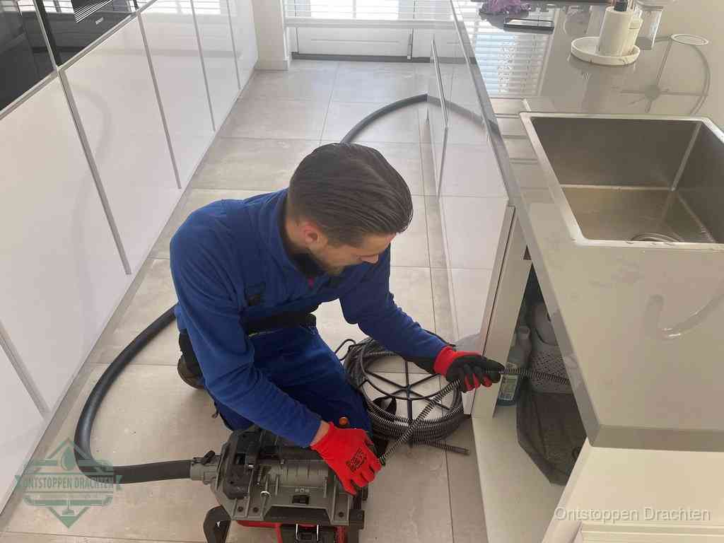 Een monteur ontstopt de keukenafvoer onder de spoelbak met een elektrische veermachine in Drachten