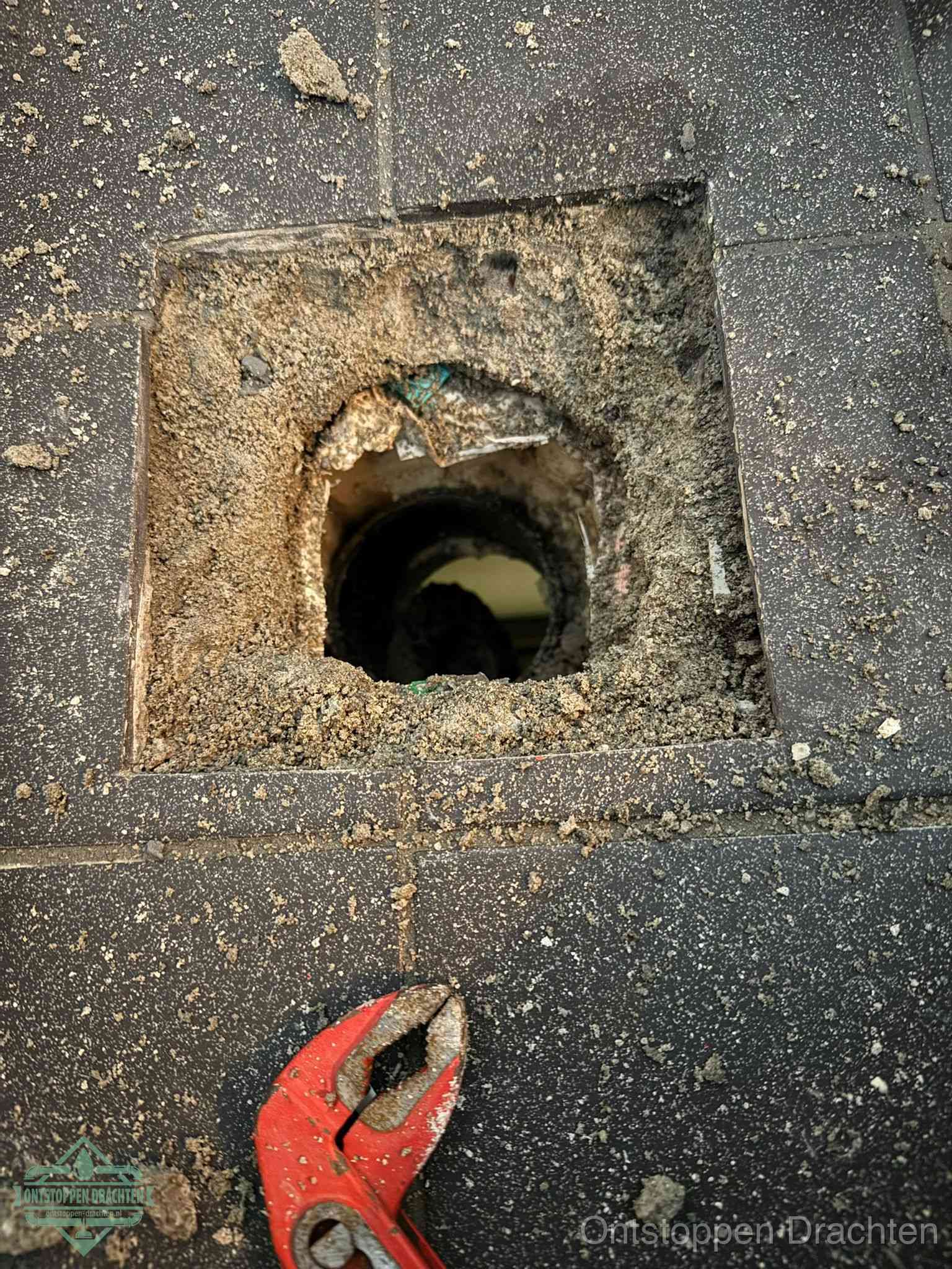 Een geopend rioolputje in een betontegelvloer met losgemaakt rooster en een zichtbare ronde afvoerbuis, het achterhalen waar de afvoerverstopping zit in Drachten
