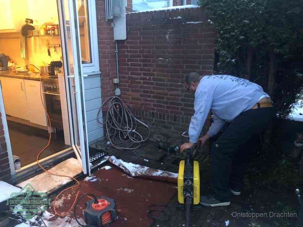 Een monteur werkt buiten bij een open riool-/grondput met een elektrische ontstoppingsmachine om een verborgen afvoerprobleem op te sporen in Drachten