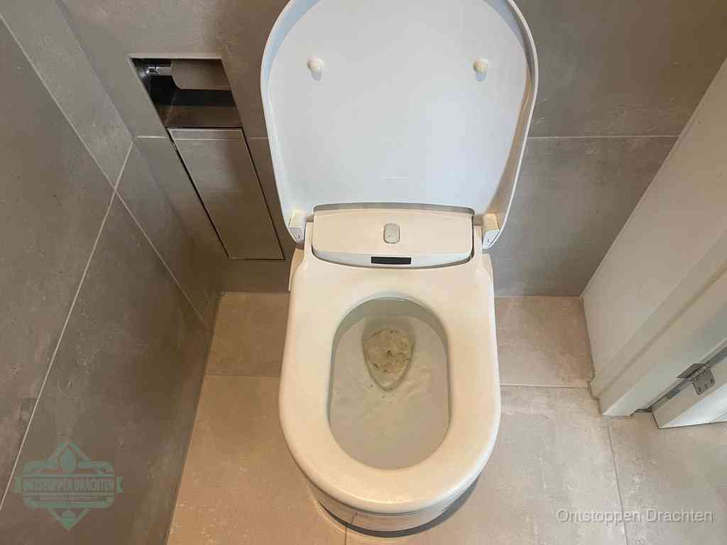 Een wit hangtoilet waarin een prop wc-papier op het water blijft drijven, een duidelijk signaal van een verstopte wc in Drachten