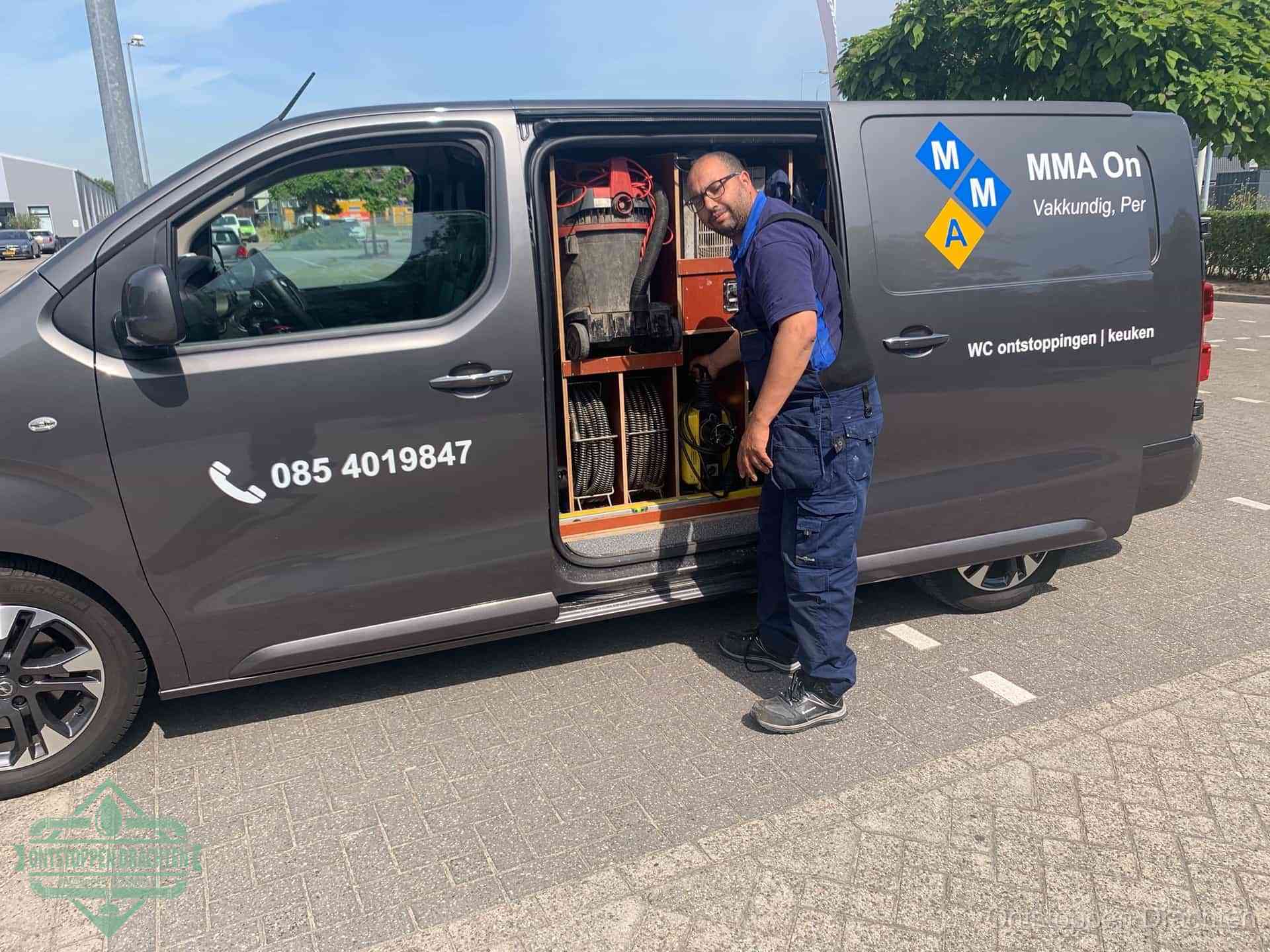 Een monteur bij de open schuifdeur van zijn bedrijfsbus op een parkeerplaats, klaar om de oorzaak van terugkerende afvoerverstoppingen aan te pakken in Drachten