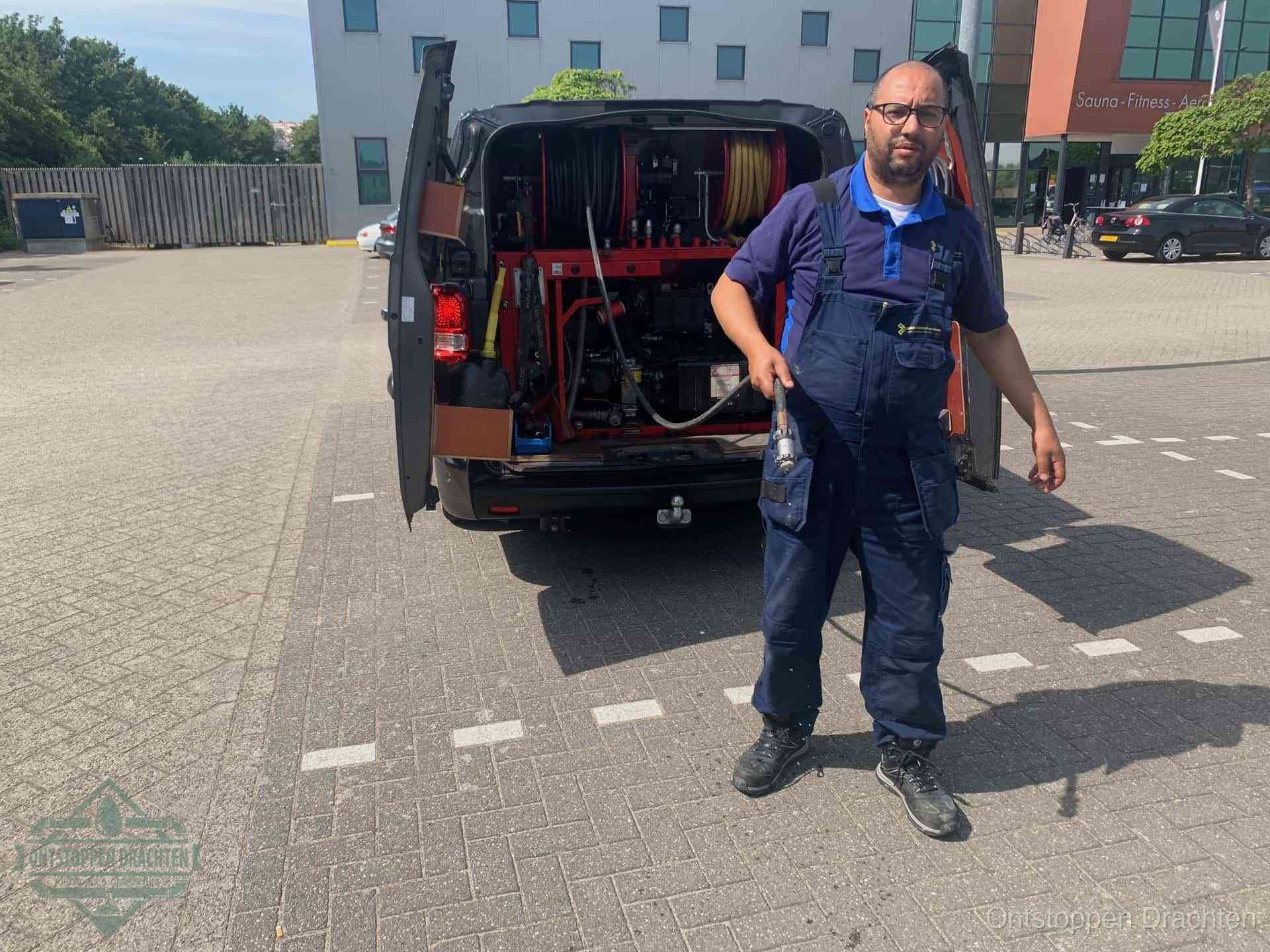 Een monteur bij zijn bestelbus met een hogedruk- en rioolreinigingsunit, klaar om de oorzaak van terugkerende wc-verstoppingen aan te pakken in Drachten