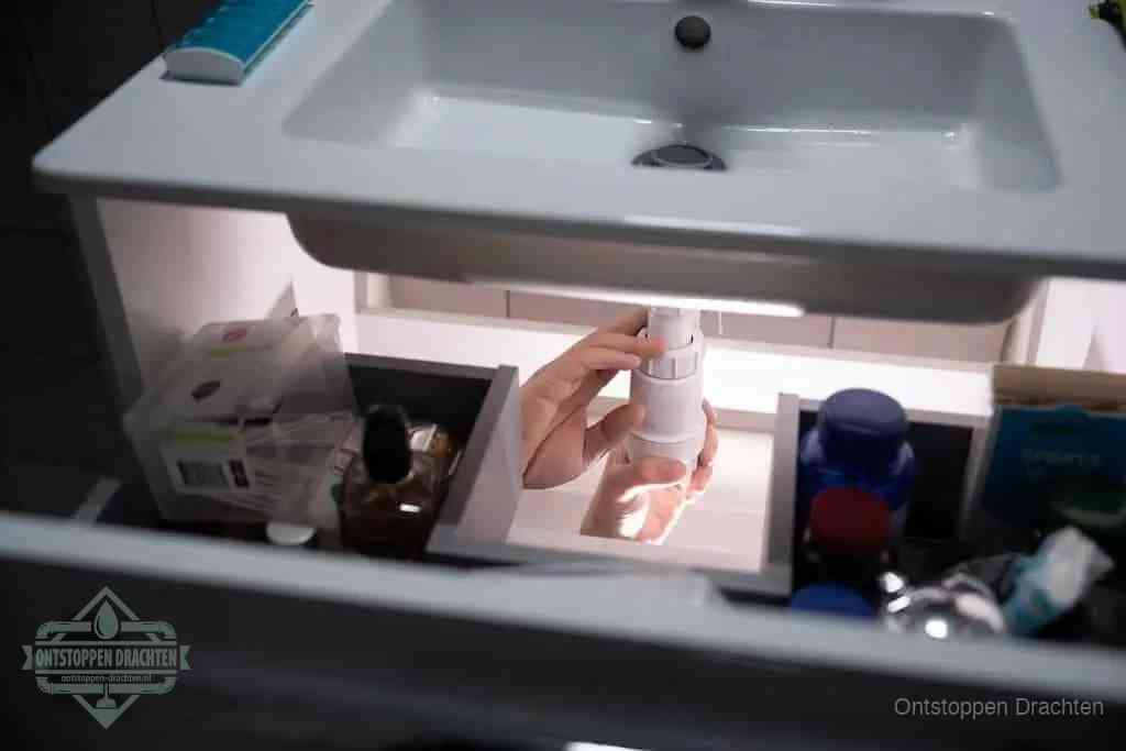 Een pompfles met zeep boven een wastafel in de toiletruimte, de warm water en afwasmiddel-methode om de wc te ontstoppen in Drachten