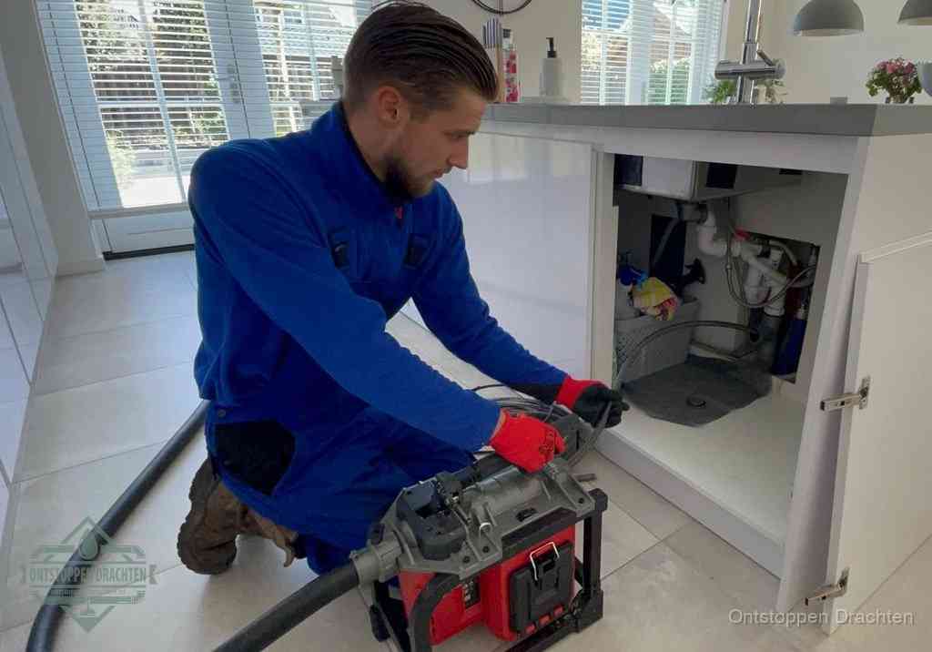 Een monteur voert een professionele elektrische ontstoppingsmachine in de afvoer onder de spoelbak tijdens het gootsteen ontstoppen in Drachten